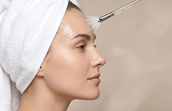 Side profile of woman receiving chemical peel or gel mask application with fan brush on forehead