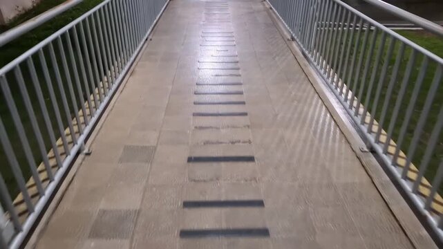 A slow forward camera movement perspective of an empty outdoor pedestrian overpass walkway with metal railings at night.