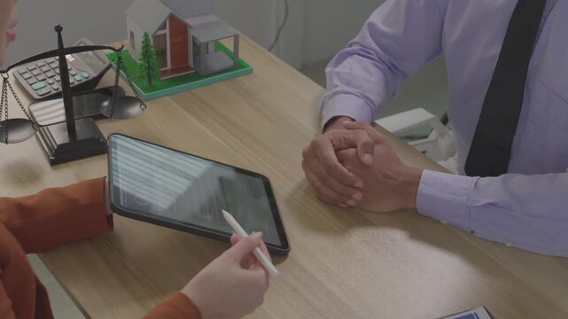 A real estate agent is presenting a digital home purchase agreement to a client on a tablet, along with a house model and concepts related to property law.
