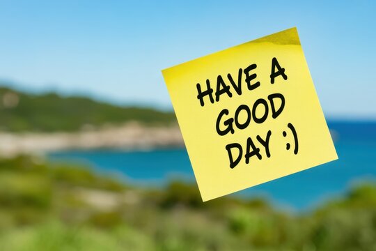 Yellow sticky note with handwritten HAVE A GOOD DAY message and smiley face against a blurry coastal landscape background