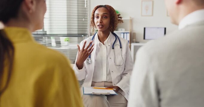 Doctor meets couple for pregnancy planning consultation. In a healthcare clinic, a physician reviews options with the young family, providing practical advice. Happy couple gets clear advice.