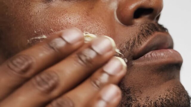 Close up of a Black man applying a thick yellow cream to his cheek. Focus on skin texture and grooming routine. Ideal for beauty, skincare, and male self care content.