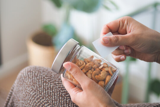 A person putting a label on a glass jar of cashews at home