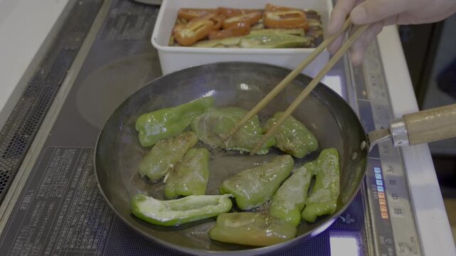 煮浸し調理で緑色のピーマンを鉄フライパンから取り出し、容器のつけ汁に入れるシーン
