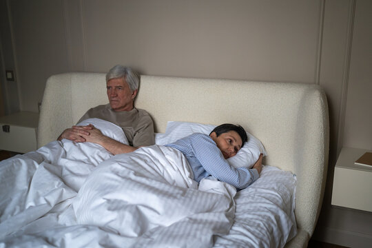 Exhausted elderly married lying in bed with frustration and disappointment after arguing, senior husband and wife holding out offence and disagreement, partners growing apart after crisis.