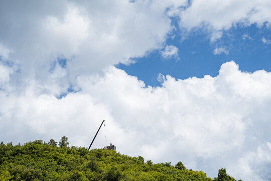 Crane and construction tower on green forested hill under dramatic cloudy sky