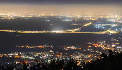 Fototapeta premium Aerial shot of a beautifully lit town and busy highway night landscape - View of illuminated houses and highway traffic streaks at night