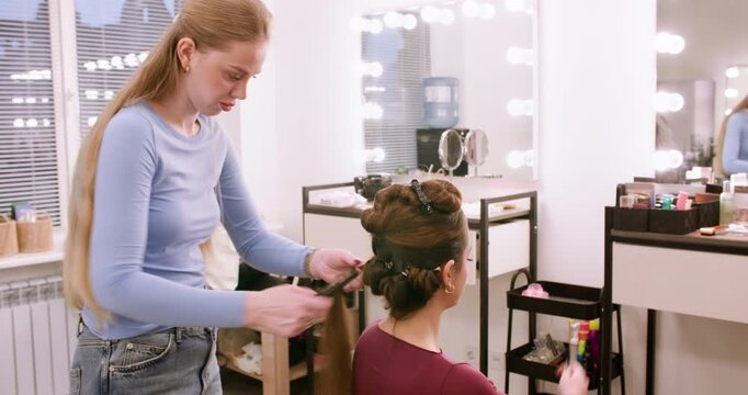 Salon service. Hairdo styling. Woman professional hairstylist creating curls using curling irons comb in beauty workplace indoor.