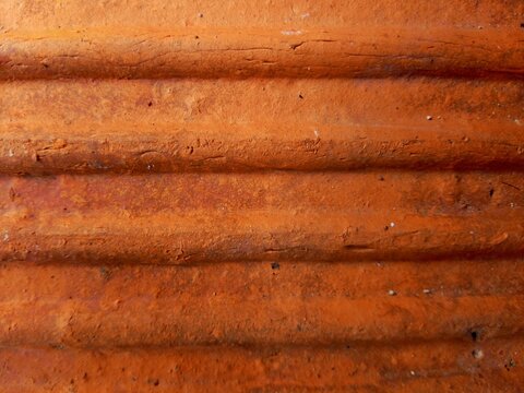Close up texture of orange terracotta roof tile with wavy ridged surface 