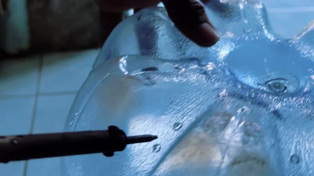 A person inflates a clear plastic object with a pump on a tiled floor.