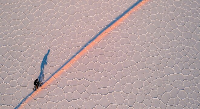 Cyclist riding bicycle on dry salt flats creating long shadow at sunset