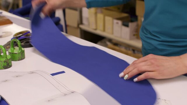 Dressmaking process. Clothing production. Female seamstress folding cut blue fabric pattern draft on table with tailor professional tool.