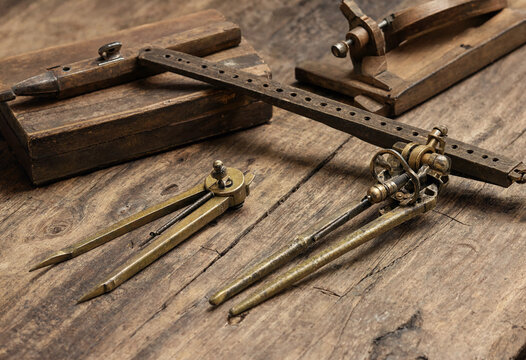 Antique brass drafting and measuring tools including compasses and a wooden ruler on a rustic dark wooden table surface background