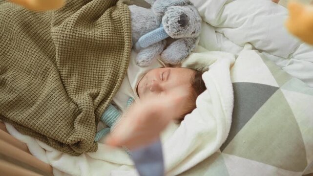 Baby boy sleeping in a crib with knitted bunny and olive blanket, eyes closed and face relaxed in a nursery; serenity.