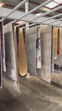 Rows of patterned rugs hang from white metal racks in a spacious storage showroom, creating a neat aisle with layered textile textures, neutral tones,