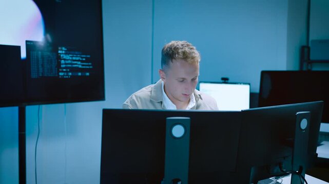 Concentrated IT specialist monitoring data code on multiple computer screens inside a futuristic security operations center with blue lighting