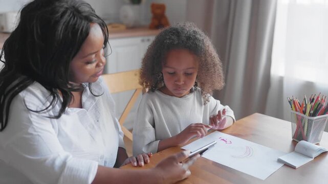 Drawing lesson or session with neuropsychologist for kids, tutor showing video. African american woman and cute black girl watching tutorial on smartphone display, education for preschoolers or pupils