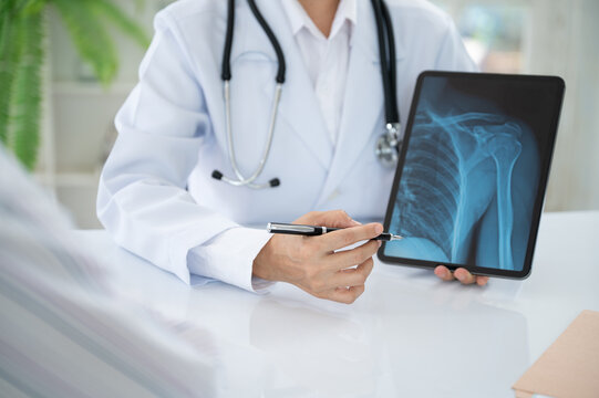doctor radiologist explain to the patient about shoulder joint x-ray images on digital tablet to see injuries of tendons and bones.