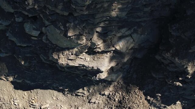 Exposed rock layers and loose rubble on the steep wall of an active quarry. The excavated slope reveals geological strata, fractured stone, and raw mineral deposits in an industrial extraction site.