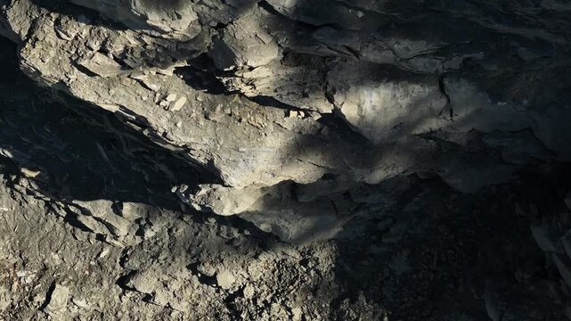 Exposed rock layers and loose rubble on the steep wall of an active quarry. The excavated slope reveals geological strata, fractured stone, and raw mineral deposits in an industrial extraction site.