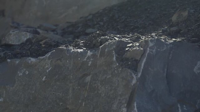 Close-up of a cut stone edge in a quarry with loose gravel and fragmented rock. The image highlights extraction marks, rough textures, and exposed mineral material in an active excavation site.