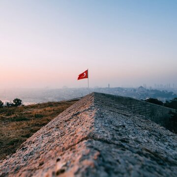 Weathered stone parapet leading toward a red national flag on a hilltop at sunrise for city editorial, travel marketing and national pride campaigns during dawn light