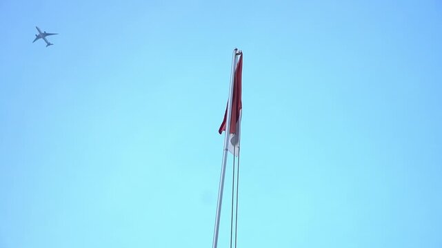 Small airplane flying through clear blue sky past national flag
