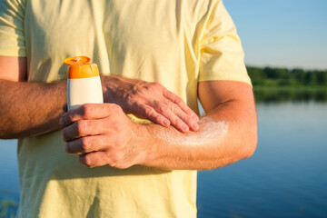 Obraz premium Man applies SPF sunscreen to arm in sunny outdoor setting near water. Concept: UV protection, summer skincare, sun safety