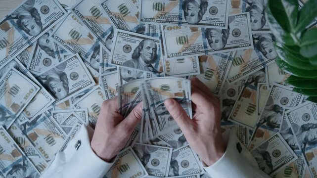top view of a man's hands counting a large stack of cash over a pile of money on a desk