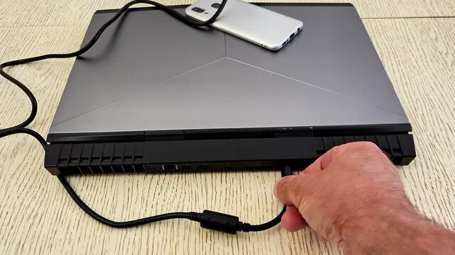 Person disconnects laptop charger from rear port, highlighting power supply, device care, workspace setup, and everyday computing tasks in a modern technology environment