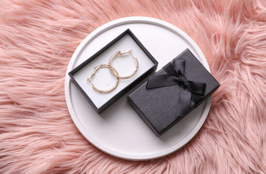 Gold earrings with box on a plaster podium, pink background