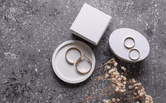 Gold earrings and rings in tray with jewelry box on concrete background