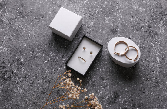 Gold earrings and rings in tray with jewelry box on concrete background