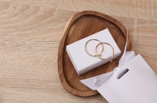 Gold earrings with white jewelry box in tray on table