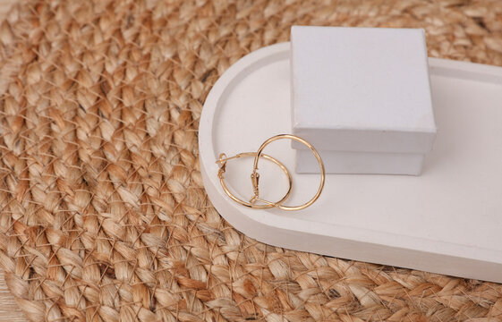 Gold earrings with box in a plaster tray on a woven straw mat. Jewelry product presentation