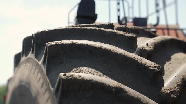 Detailed close up of large agricultural tractor tire covered with soil and dust. Farming machinery working during field cultivation and crop production.