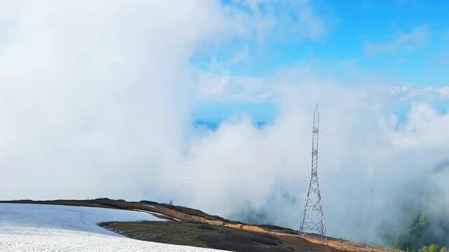 Mountain pass with snow patch under thick thick clouds and high voltage towers .