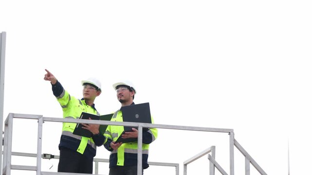Professional Asian renewable energy experts planning ecological turbine system project inside farm. Two industrial safety technicians reviewing green clean electricity power.