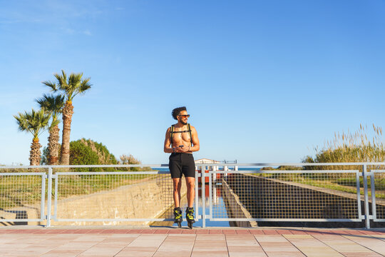 Shirtless man wearing rollerblades and sunglasses checking phone outdoors
