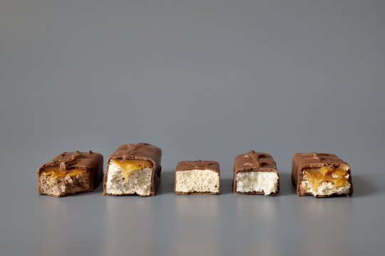 Five broken chocolate bars with different visible fillings isolated on a gray background, showcasing confectionery variety, textures, and product selection concepts