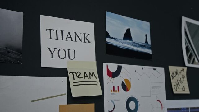 Close-up shot of office board displaying sticky notes with handwritten Thank You Team message alongside business charts and infographics. Corporate culture and employee appreciation videos