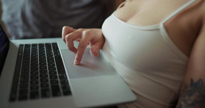 Extreme close up of a young woman in singlet, her finger using laptop trackpad at home
