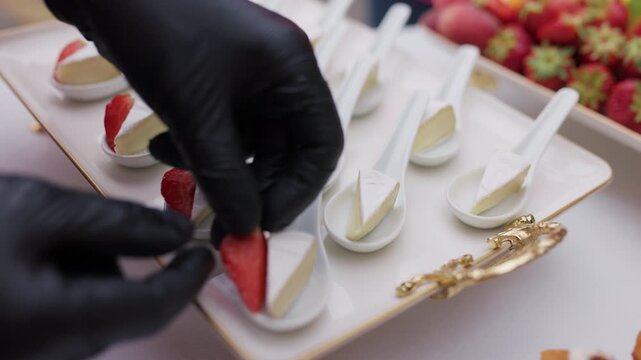 Catering chef in black gloves arranging brie cheese and strawberry appetizers