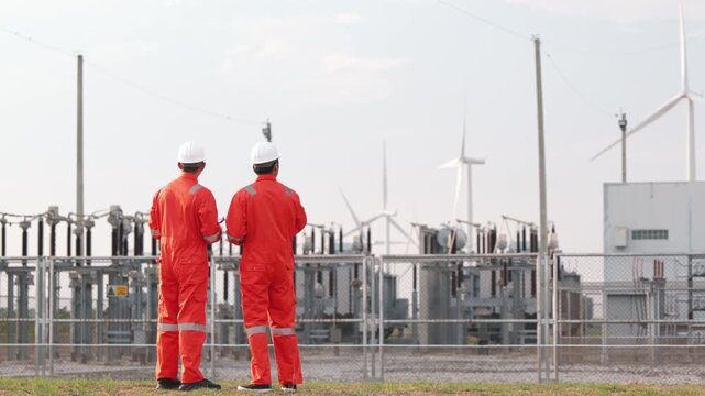 Corporate Asian power technicians cooperating near alternative turbine grid network layout field. Technical safety workers checking renewable green electricity system outdoor.