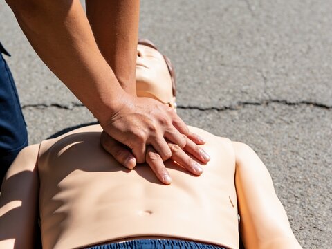 A close-up view of a person performing CPR compressions on a medical training dummy on the ground.