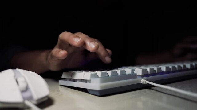 Hands typing on white mechanical keyboard in dark workspace, Close-up of hands typing on a white mechanical keyboard with a white mouse on desk