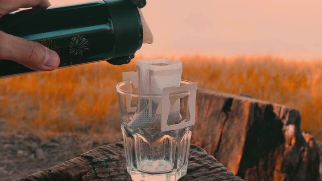 Pouring hot water from a kettle for drip coffee by the lake during morning camping trip