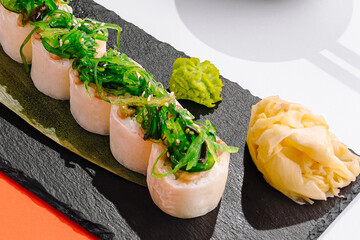 Delicious maki sushi rolls wrapped in rice paper are served on stone plate. Healthy Asian appetizer is topped with vibrant green wakame seaweed salad. © AntAlexStudio