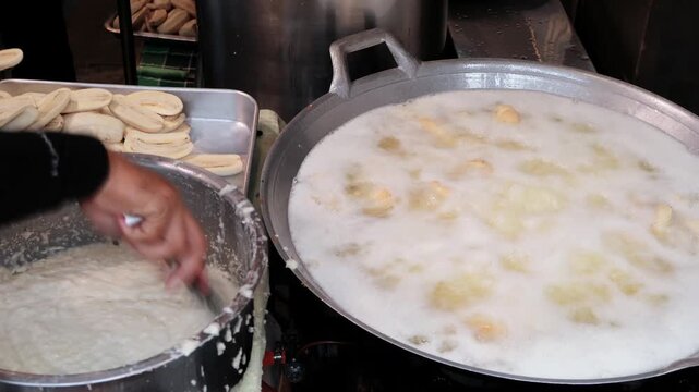Street food vendor mixing sliced bananas in flour coconut batter with a boiling frying pan in front