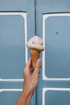 Summer Bliss: Close-Up of a Hand Holding a Flavorful Ice Cream Cone Against a Bright Blue Wall